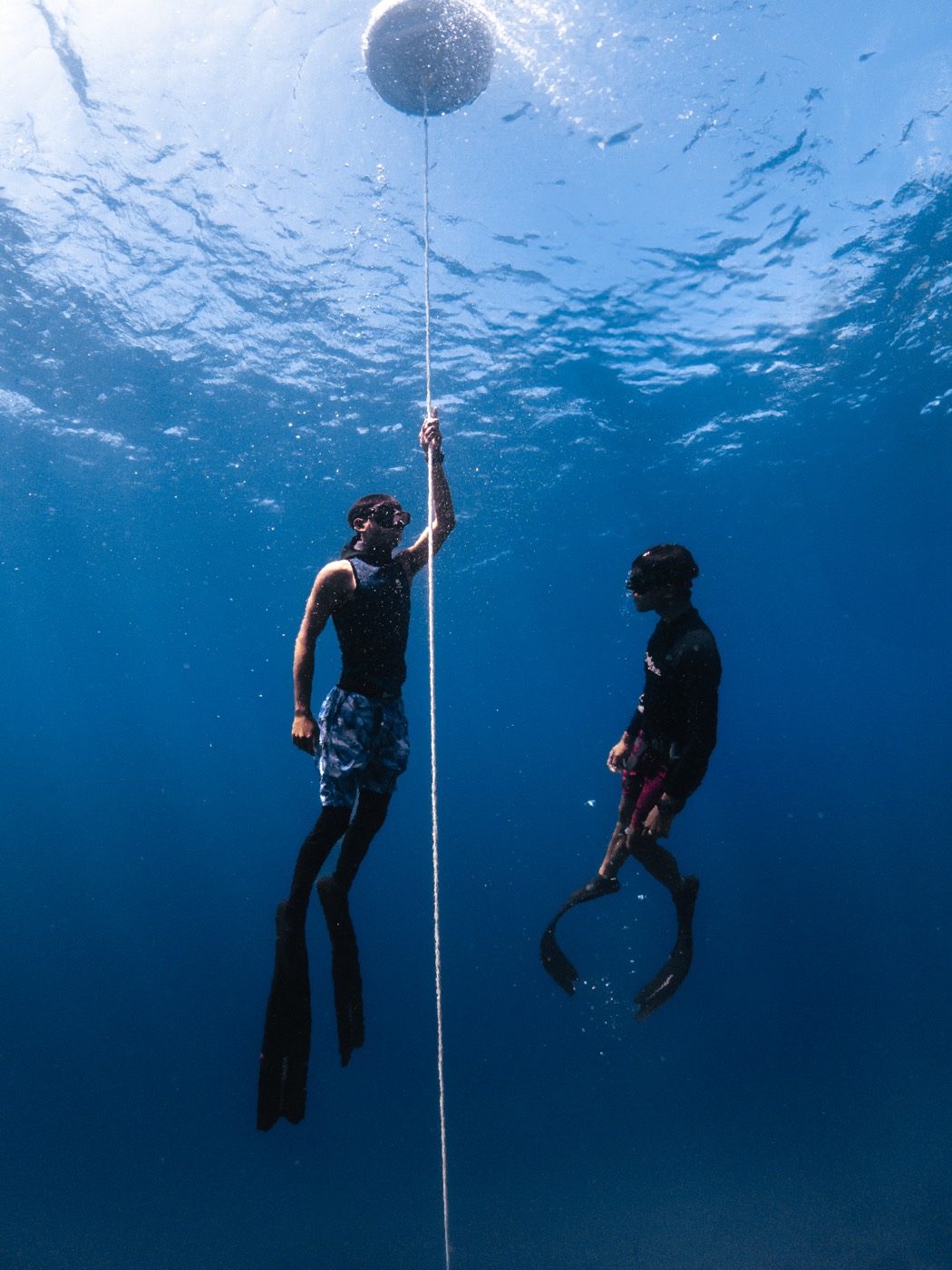 Two freedivers descending a line into the deep blue off Maratua